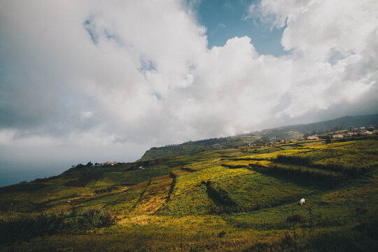 Rolling green hills and terraced fields under a massive, dramatic sky filled with heavy white clouds