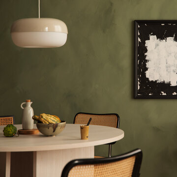 Modern minimalist dining room interior with round wooden table, rattan chairs, pendant lamp, and abstract art piece against a dark green wall