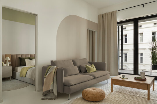 Modern minimalist living room interior with neutral colors, comfortable sofa, coffee table, and an open view into the bedroom