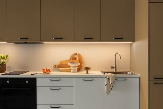 Modern minimalist kitchen interior design with white and olive green cabinets, wooden cutting boards, sink, and warm under-cabinet LED strip lighting
