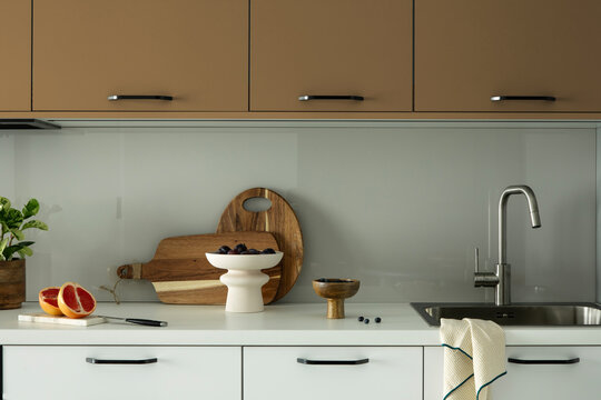 Modern minimalist kitchen interior with wooden cutting boards, fruit bowl, sink, and stylish taupe and white cabinets for home decor design
