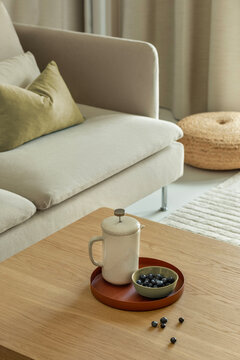 Cozy living room interior with a comfortable beige sofa, wooden coffee table, ceramic coffee press pot, and fresh blueberries on a tray