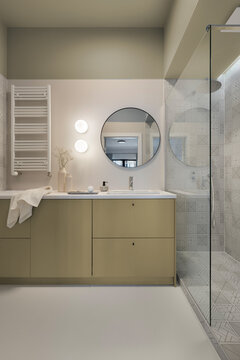 Modern minimalist bathroom interior design with beige vanity cabinet, round mirror, glass shower enclosure, and warm ambient lighting setup