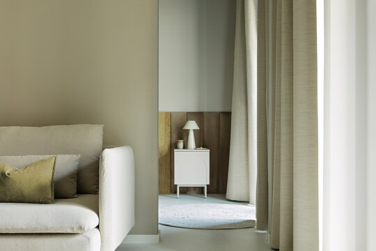 Minimalist living room interior with modern beige sofa, stylish table lamp, and soft neutral curtains creating a calm and serene atmosphere