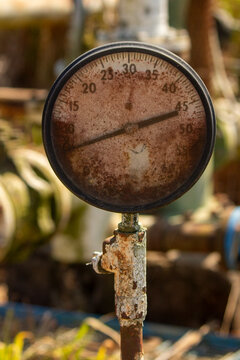 Rusty old industrial pressure gauge meter on pipe with blurred factory background