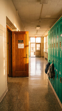 School hallway with open wooden door leading to art room, lined with green lockers, symbolizing education and learning environments