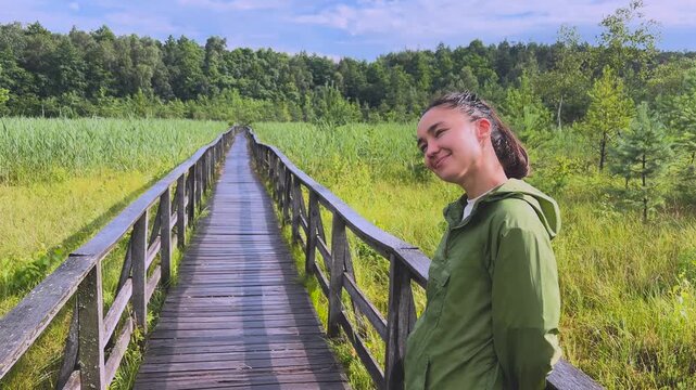 Young woman walking along a wooden boardwalk in a national park turning back and smiling at the camera