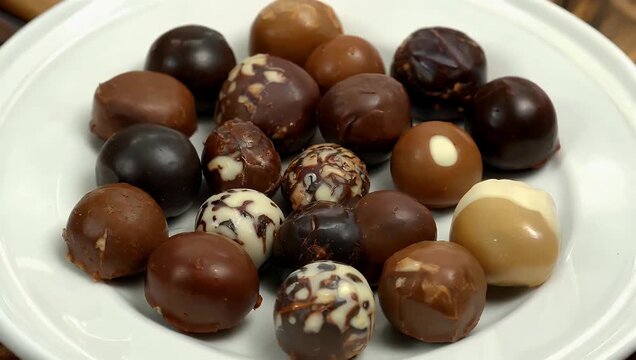 Delicious 4K UHD overhead rotating shot presenting an exquisite assortment of handcrafted gourmet dark chocolate truffles and praline candies elegantly arranged on a bright white porcelain plate for