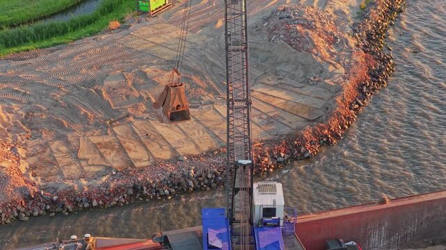 Crane unloading sand onto barge for dike reinforcement construction