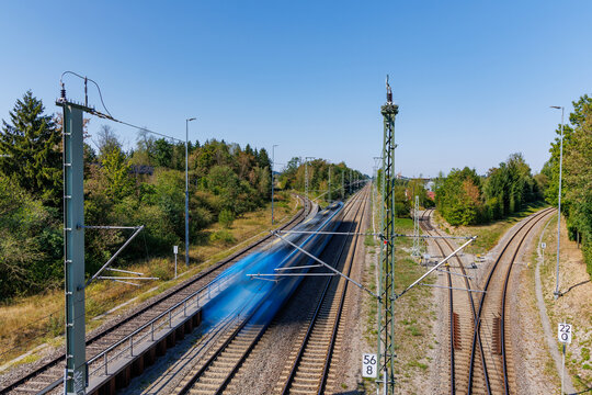 High angle view of motion blurred fast passenger train moving on railway tracks under blue sky, electric rail transport and speed concept