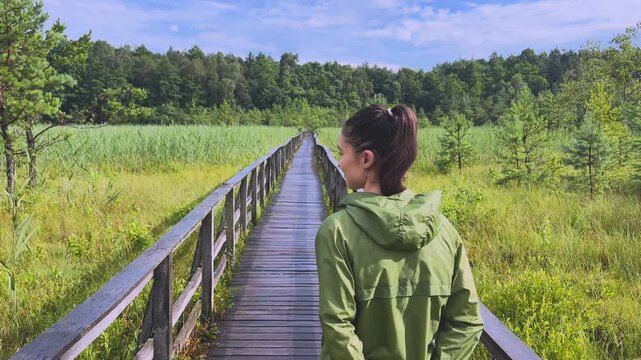 Young woman walking along a wooden boardwalk in a national park turning back and smiling at the camera