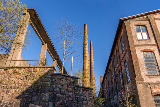 Old abandoned factory building with tall brick chimneys and concrete beam structure under clear blue sky, industrial heritage and lost places concept