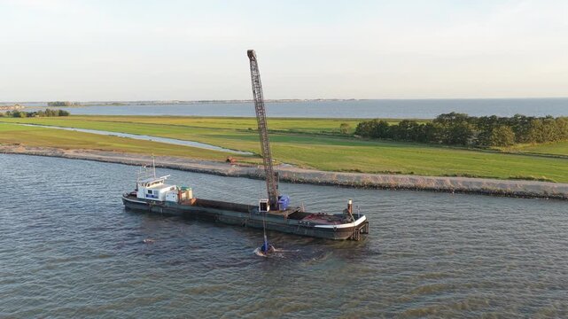 Dredging barge with crane performing dike reinforcement work in netherlands