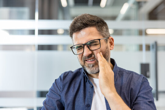 Man experiencing dental pain and discomfort, grimacing while pressing hand against his cheek, conveying a concept of oral health issues and needing medical attention