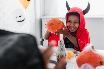 Fototapeta premium Little boy in vibrant Halloween costume smiling while holding a carved pumpkin