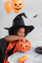 Fototapeta premium Little girl joyfully preparing a Halloween pumpkin in her vibrant costume