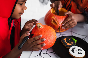 Fototapeta premium Kids enjoying Halloween fun by carving pumpkins and decorating cookies at home
