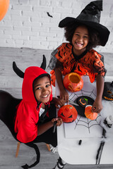 Fototapeta premium Joyful siblings crafting Halloween decorations in colorful costumes