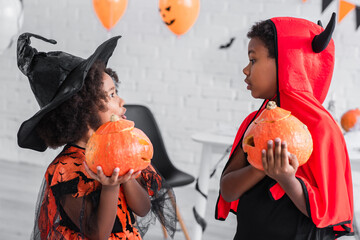 Fototapeta premium Joyful siblings celebrate Halloween in vibrant costumes with carved pumpkins