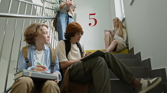 Caucasian teenagers sitting on school stairs, discussing lessons and writing in notebooks. Clip is perfect for high school marketing and educational service advertisements