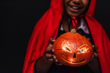 Fototapeta premium Cute little African American boy in colorful Halloween costume with spooky pumpkin