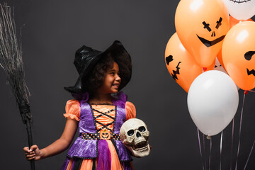Fototapeta premium Little girl in vibrant witch costume celebrating Halloween with spooky balloons