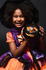 Fototapeta premium Little girl in a vibrant Halloween costume joyfully holding a spooky pumpkin