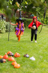 Fototapeta premium Joyful siblings celebrate Halloween in colorful costumes while running in a sunny backyard