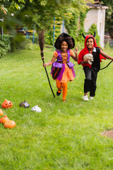 Fototapeta premium Little siblings in vibrant Halloween costumes share joy in a sunny autumn garden
