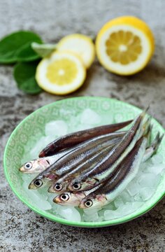Close-up of a stack of fresh anchovies on ice in a bowl with fresh lemon