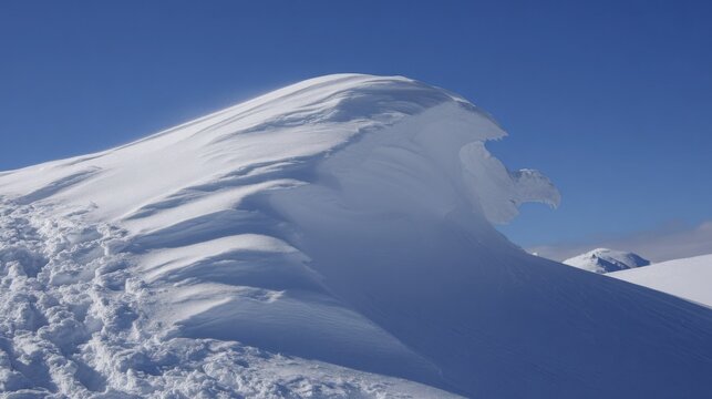 Dramatic snow cornice formation sculpted by wind on a high mountain ridge under a clear blue sky.
