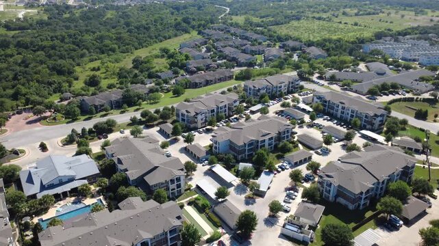 Pitched roof apartment communities face South Congress Avenue extensions. Sparkling outdoor pools, extensive vehicle parking stalls, green parkland reflect suburban living, Austin, Texas