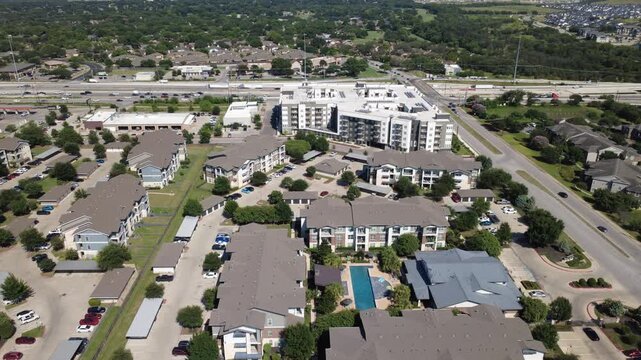 Multi building residential villages border Interstate 35 highway corridors. Central swimming pools, open parking plazas, distant commercial hubs present energetic metro growth, Austin, Texas. USA