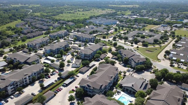 Multi tier apartment buildings cluster near Onion Creek neighborhood parkways. Paved vehicle courts, swimming pools, tree lined thoroughfares emphasize South Texas housing growth, Austin, Texas