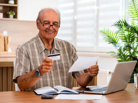Portrait of happy senior man using laptop to review savings, investments and financial information while planning his home finances.