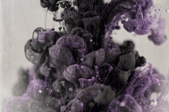 Abstract purple and black ink swirling in water creates dynamic fluid patterns against a bright background