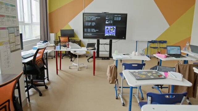 Empty modern classroom with computer desks and large interactive screen displaying programming code, camera zooming in slowly. Clip is suitable for educational marketing or school promotions