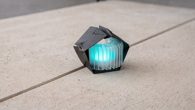 Modern Geometric Paper Origami Lamp with Glowing Cyan LED Light on Concrete Surface