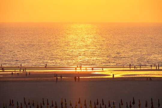 Silhouettes of people and parasols on the beach of Deauville at sunset in summer, Normandy, France. Aerial view and golden sunset light
