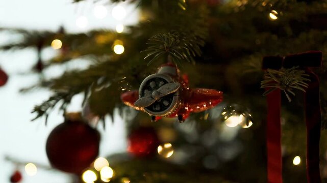 Retro toy plane bauble decorating a green Christmas tree branch with warm glowing holiday fairy lights in the background.