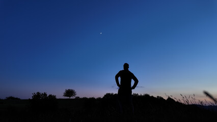 Silhouette of a person in nature observing night sky, Moon, stars and planets from a remote location. © astrosystem