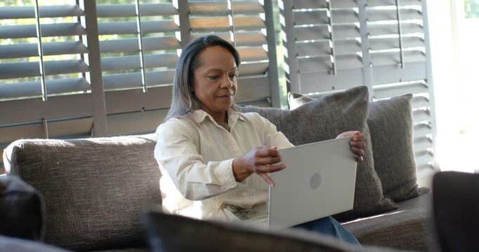 Mature woman gesturing then closing laptop ending online call, resting on sofa with watch