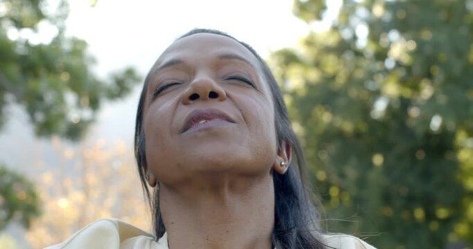 Mature African American woman tilting back closing eyes breathing wearing studs outdoors for calm