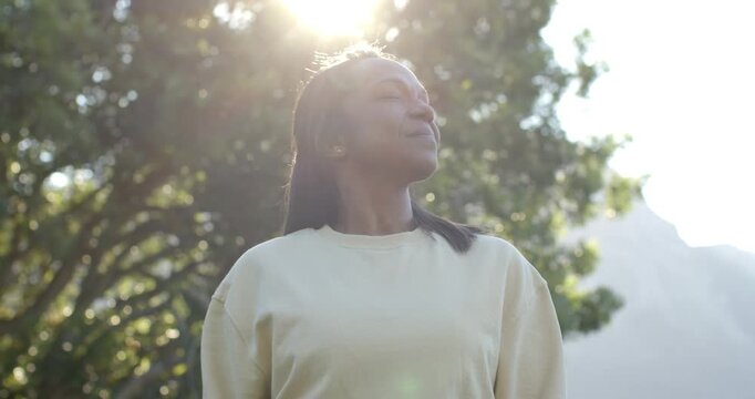 Mature African woman tilting head up in park sun backlit causing closing eyes breathing lens flare