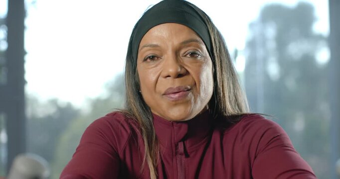 Mature African American woman leaning forward giving tip to camera at home window in maroon jacket