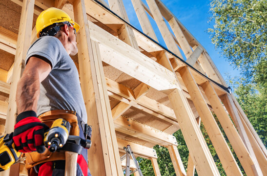 Construction worker holds drill and looks at building frame