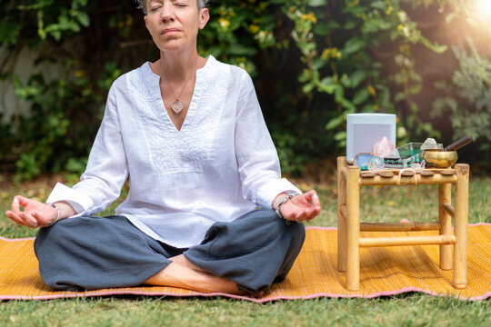 Woman meditating outdoors beside a Schumann wave generator and healing crystals, cultivating mindfulness, emotional balance, relaxation, and spiritual wellbeing in a peaceful natural setting.