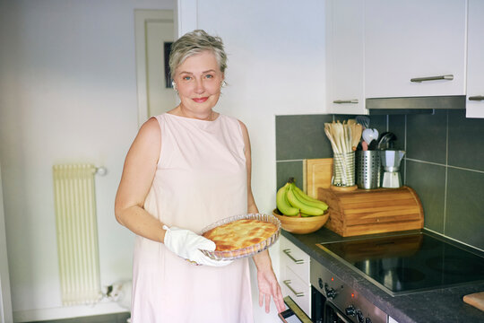 55-60 Year Old Woman Holding Fresh Homemade Pie in Modern Kitchen, Smiling Mature Female Cooking and Baking Food at Home