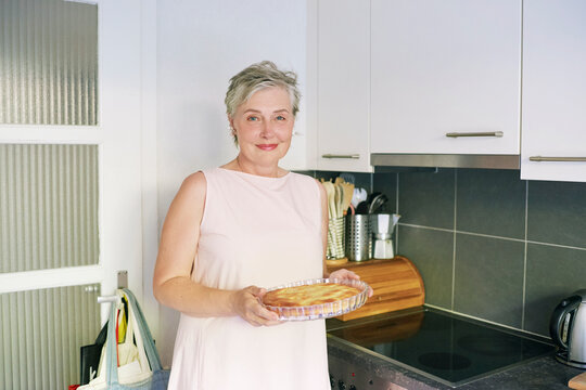 55-60 Year Old Woman Holding Fresh Homemade Pie in Modern Kitchen, Smiling Mature Female Proud of Her Baking and Enjoying Cooking Food at Home