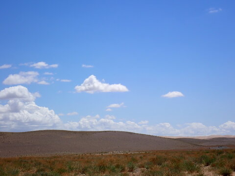 Vast open landscape in Mongolia featuring barren rolling hills, dry grassland, and a blue sky with scattered clouds.